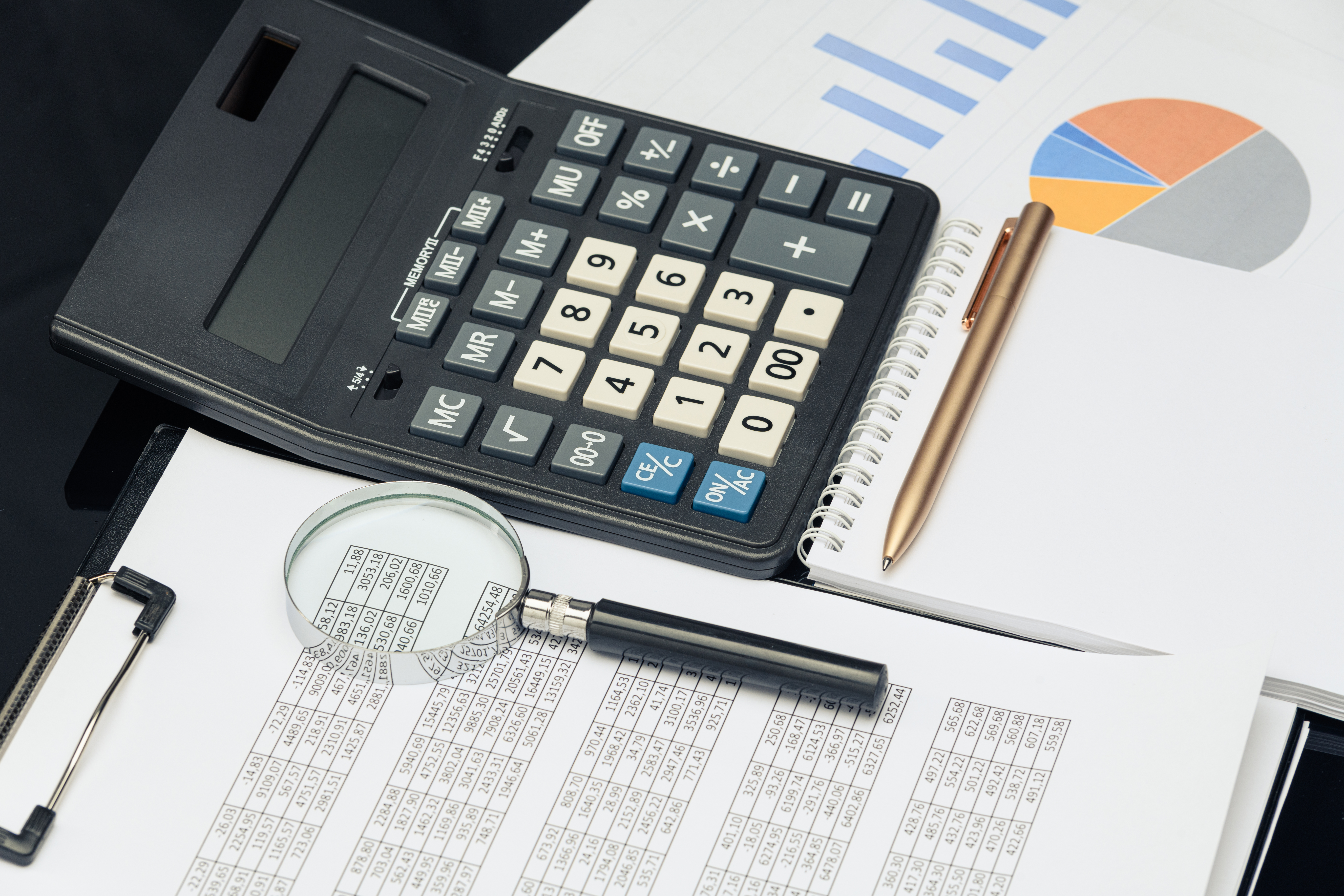 Business financial documents, office calculator and pen on the table. Numbers and graphs. Black table
